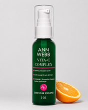 Load image into Gallery viewer, Ann Webb Vita-C Complex 2 oz pump bottle in dark green with a white cap, shown next to a halved orange on a light gray background.