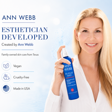 Load image into Gallery viewer, A smiling blonde woman in a white blouse holds a blue spray bottle of Ann Webb Hair Plus Mist against a bright light blue background with product marketing text on the left.

