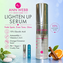 Load image into Gallery viewer, Ann Webb Skin Care Lighten Up Serum bottle shown prominently on a blue-to-white gradient background with product claims, a small sample vial, a pump bottle, and orange/cinnamon props.
