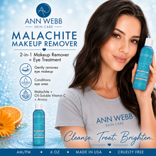 Load image into Gallery viewer, A woman holds a bottle of Ann Webb Skin Care Malachite Makeup Remover next to a large product label on a light blue background. She is wearing a gray t-shirt with the brand name printed on it, and an orange slice and flower are visible in the lower left corner.

