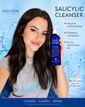 Load image into Gallery viewer, A woman holding a bottle of Ann Webb Salicylic Cleanser against a blue water-themed background with product text and benefits.
